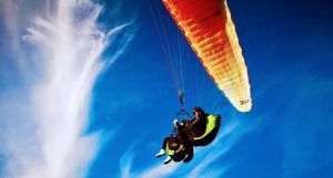 Parapentes biplaza bajo un dosel naranja se deslizan a través de tenues nubes y un cielo azul intenso cerca de la pintoresca ciudad de Vejer en Cádiz, experimentando el "Vuelo en parapente biplaza en Vejer (Cádiz). - ForTwo - Planes para parejas