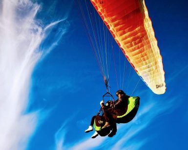 Parapentes biplaza bajo un dosel naranja se deslizan a través de tenues nubes y un cielo azul intenso cerca de la pintoresca ciudad de Vejer en Cádiz, experimentando el "Vuelo en parapente biplaza en Vejer (Cádiz). - ForTwo - Planes para parejas