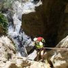 Vestido con equipo de escalada, una persona desciende en rápel por el Barranco de Guardajamas, con una impresionante cascada detrás de ellos, personificando la emoción del Barranquismo en Granada. - ForTwo - Planes para parejas