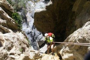 Vestido con equipo de escalada, una persona desciende en rápel por el Barranco de Guardajamas, con una impresionante cascada detrás de ellos, personificando la emoción del Barranquismo en Granada. - ForTwo - Planes para parejas