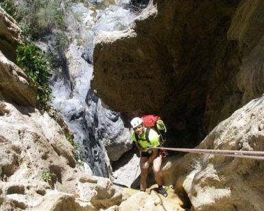 Vestido con equipo de escalada, una persona desciende en rápel por el Barranco de Guardajamas, con una impresionante cascada detrás de ellos, personificando la emoción del Barranquismo en Granada. - ForTwo - Planes para parejas