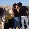 Una pareja comparte un beso entre dos caballos blancos ensillados en una ladera pintoresca durante el "Paseo a caballo por la sierra de Guadarrama con picnic para dos". - ForTwo - Planes para parejas