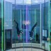 Dos personas con cascos saltan en paracaídas en el interior de Windobona Indoor Skydiving Madrid, en un túnel de viento cilíndrico con vibrantes luces verticales. - ForTwo - Planes para parejas