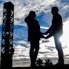 Una pareja de siluetas cogidas de la mano bajo un cielo nublado de Barcelona con árboles y estructuras al fondo ejemplifica maravillosamente la Sesión de fotografía romántica al aire libre (Barcelona). - ForTwo - Planes para parejas