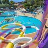 Vista aérea del parque acuático Isla Fantasía en Barcelona destaca emocionantes toboganes y piscinas; una mujer disfruta de un tobogán morado. Texto: Nuevas atracciones 2019, Entradas para el parque acuático Isla Fantasía (Barcelona). - ForTwo - Planes para parejas