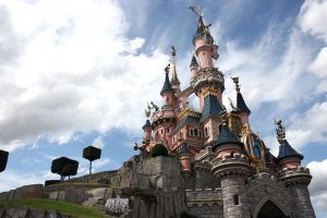 Un majestuoso castillo rosa con torres se yergue orgulloso bajo un cielo azul salpicado de nubes esponjosas, que recuerda una escena sacada directamente de una excursión a Disneyland París desde París. - ForTwo - Planes para parejas