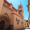 Una calle estrecha con una gran iglesia ornamentada y un campanario imponente bajo un cielo azul brillante, que ofrece el ambiente encantador del Barrio de Triana de Sevilla, como se experimenta en el "Tour gratuito por el barrio de Triana (Sevilla). - ForTwo - Planes para parejas