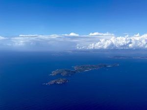 Experimente la impresionante vista de una exuberante isla verde rodeada por el océano azul profundo bajo un cielo despejado con nubes dispersas, como si volara en una "Sobrevuela en avión las Islas Cíes (Vigo)", capturando el encanto encantador de las Islas Cíes cerca de Vigo. - ForTwo - Planes para parejas