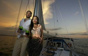Una pareja disfruta de un romántico paseo en barco en la Herradura y Almuñécar, tomando bebidas mientras se deslizan por aguas serenas con velas puestas contra la vibrante puesta de sol. - ForTwo - Planes para parejas