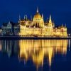 El edificio junto al río iluminado por la noche crea reflejos románticos en el agua, creando una escena pintoresca perfecta para el "Romántico paseo en barco al anochecer (Budapest)". - ForTwo - Planes para parejas