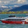Un barco turístico ofrece un encantador "Paseo en barco en Santander" en un lago sereno, con montañas nevadas y exuberantes colinas verdes que evocan la belleza de Santander en el fondo. - ForTwo - Planes para parejas