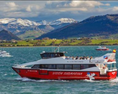 Un barco turístico ofrece un encantador "Paseo en barco en Santander" en un lago sereno, con montañas nevadas y exuberantes colinas verdes que evocan la belleza de Santander en el fondo. - ForTwo - Planes para parejas