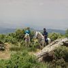 Dos personas disfrutan de un paseo a caballo por la ladera de una colina en Güéjar Sierra, donde las amplias vistas del valle y las lejanas montañas de Sierra Nevada crean el escenario perfecto para una inolvidable Escapada rural hípica de 2 noches a Sierra Nevada en Güéjar Sierra. - ForTwo - Planes para parejas