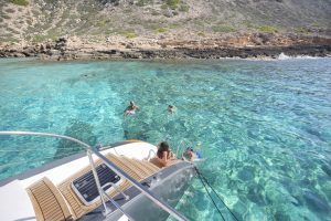 La gente nada cerca de un yate en las cristalinas aguas turquesas de una costa rocosa, ideal para "Sorprende a tu pareja con un paseo en catamarán" en Palma de Mallorca. - ForTwo - Planes para parejas
