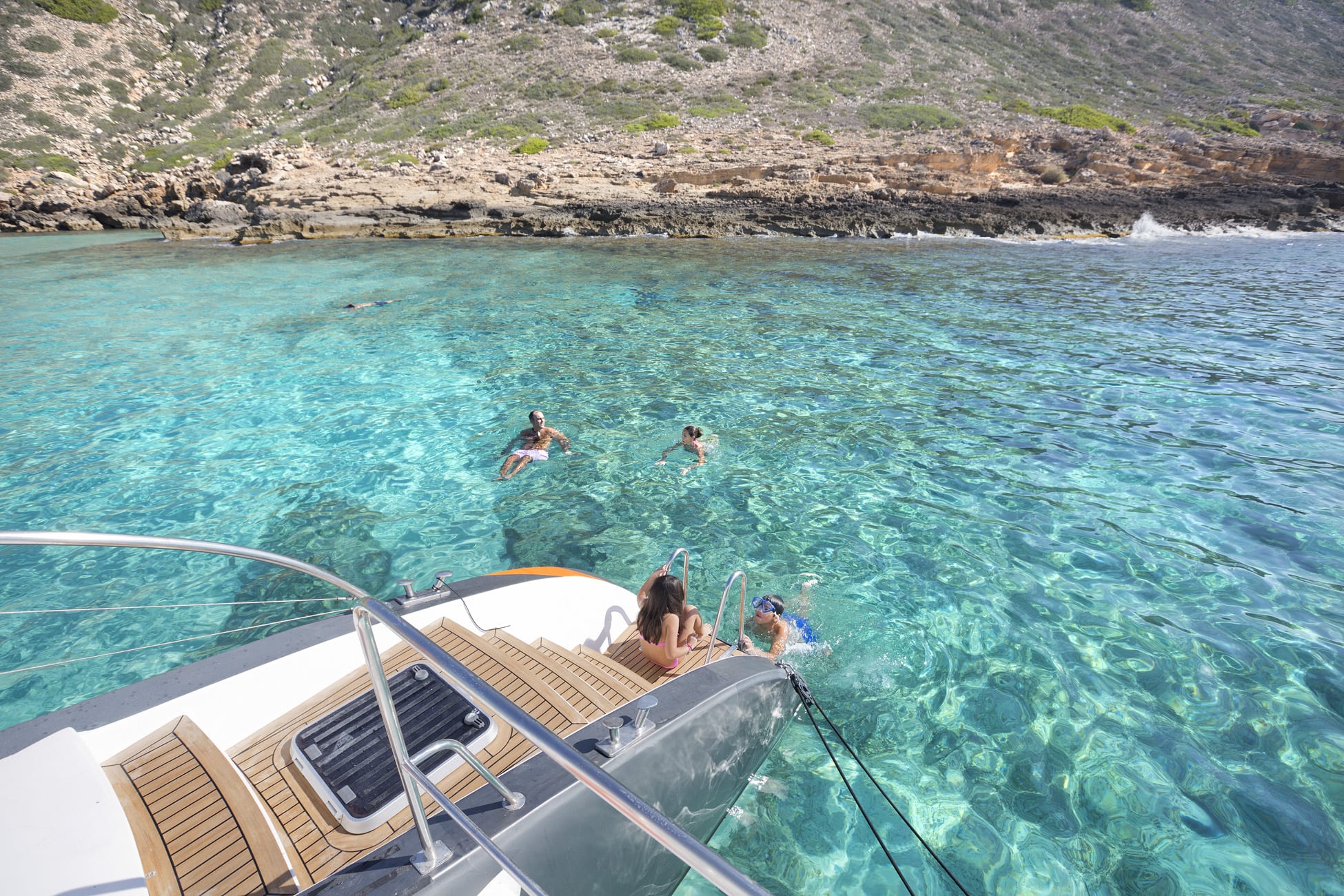 La gente nada cerca de un yate en las cristalinas aguas turquesas de una costa rocosa, ideal para "Sorprende a tu pareja con un paseo en catamarán" en Palma de Mallorca. - ForTwo - Planes para parejas