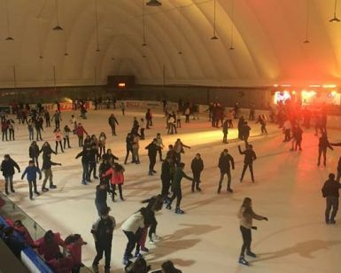 Una multitud animada disfruta de "Patinaje sobre hielo para dos en Igloo (Granada)" bajo el cálido resplandor de una pista iluminada por una cúpula, que recuerda a un iglú transportado a Granada. - ForTwo - Planes para parejas