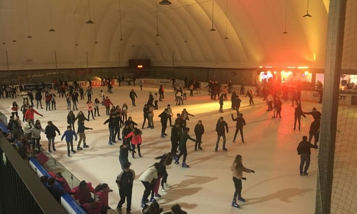 Una multitud animada disfruta de "Patinaje sobre hielo para dos en Igloo (Granada)" bajo el cálido resplandor de una pista iluminada por una cúpula, que recuerda a un iglú transportado a Granada. - ForTwo - Planes para parejas