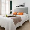 Un dormitorio minimalista exhibe una cama grande con cabecera gris y almohadas naranjas, combinada con una mesa auxiliar adornada con una lámpara y una bandeja decorativa, creando un ambiente tan tranquilo como una "Escapada con desayuno y crucero en barco por el Guadalquivir (Sevilla). - ForTwo - Planes para parejas
