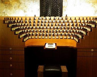 Un mostrador de madera en Crea tu perfume en El Patio de los Perfumes en Granada exhibe varios frascos de perfume pequeños, dispuestos de forma semicircular contra una pared texturizada. - ForTwo - Planes para parejas