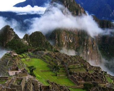 Una vista aérea de Machu Picchu muestra antiguas ruinas de piedra y terrazas verdes que se combinan armoniosamente entre picos brumosos: una imagen clásica del Viaje a Perú de 6 días. - ForTwo - Planes para parejas