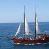 El Paseo romántico en barco de ensueño (Tenerife) se desliza con gracia sobre el océano bajo un cielo azul claro, transportando pasajeros en un viaje que captura la serena belleza de Tenerife. - ForTwo - Planes para parejas