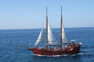 El Paseo romántico en barco de ensueño (Tenerife) se desliza con gracia sobre el océano bajo un cielo azul claro, transportando pasajeros en un viaje que captura la serena belleza de Tenerife. - ForTwo - Planes para parejas