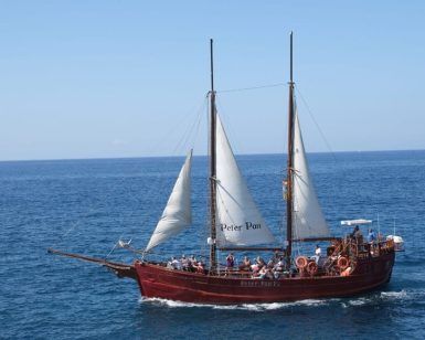 El Paseo romántico en barco de ensueño (Tenerife) se desliza con gracia sobre el océano bajo un cielo azul claro, transportando pasajeros en un viaje que captura la serena belleza de Tenerife. - ForTwo - Planes para parejas