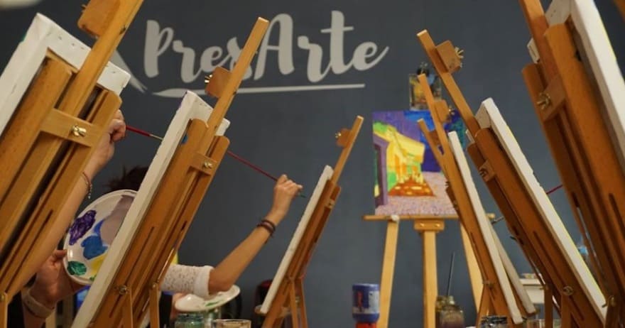 En una vibrante clase de arte, la gente pinta en caballetes debajo de la frase "Taller creativo de pintura de cuadros (Madrid)" en la pared, encarnando el espíritu de un taller creativo en Madrid. - ForTwo - Planes para parejas