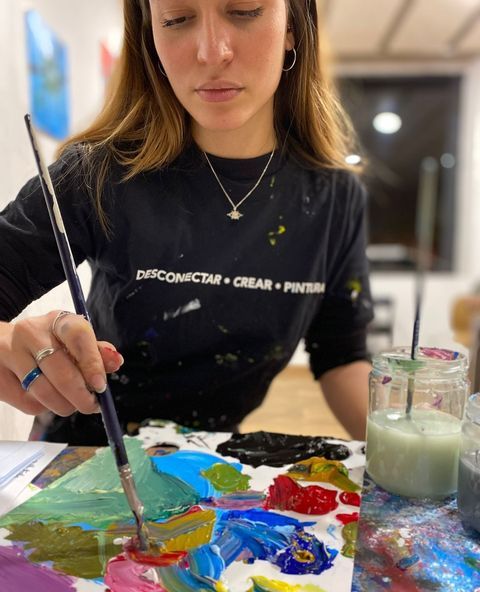 Una persona con una camisa negra y un texto creativo pinta utilizando una paleta vibrante, encarnando la esencia viva de "Clase de pintura con tu copita de vino en Arte Bar (Barcelona). - ForTwo - Planes para parejas