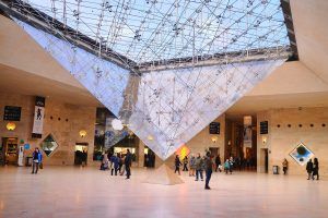 Visitantes bajo la gran pirámide de cristal invertida en el atrio del Museo del Louvre, maravillándose con la arquitectura y disfrutando de su tiempo con la Entrada para el Museo del Louvre sin hacer fila (París). - ForTwo - Planes para parejas