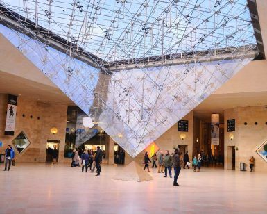 Visitantes bajo la gran pirámide de cristal invertida en el atrio del Museo del Louvre, maravillándose con la arquitectura y disfrutando de su tiempo con la Entrada para el Museo del Louvre sin hacer fila (París). - ForTwo - Planes para parejas