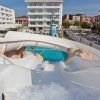 Desde la cima de un emocionante paseo en el Planazo de toboganes y almuerzo buffet en Pineda Splash 30º Hotels en Barcelona, se abre la vibrante escena; una piscina brillante debajo contrasta con edificios distantes y autos estacionados. - ForTwo - Planes para parejas