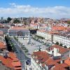 Disfrute de un tour guiado por Lisboa para apreciar plenamente la vibrante vista aérea de la plaza central de la ciudad, rodeada de edificios con techos rojos y contra un cielo azul claro, capturando el encanto de esta impresionante capital portuguesa. - ForTwo - Planes para parejas