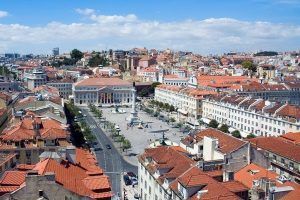 Disfrute de un tour guiado por Lisboa para apreciar plenamente la vibrante vista aérea de la plaza central de la ciudad, rodeada de edificios con techos rojos y contra un cielo azul claro, capturando el encanto de esta impresionante capital portuguesa. - ForTwo - Planes para parejas