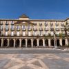 Un gran edificio con arcos y columnas, enmarcado por balcones y palmeras bajo un cielo azul vibrante, invita a la exploración a través del "Free tour por Bilbao. - ForTwo - Planes para parejas