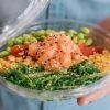 Una persona sostiene un colorido poke bowl del Restaurante Ibiza Poke, con salmón fresco, edamame, tomates cherry, maíz, algas y semillas de sésamo. - ForTwo - Planes para parejas