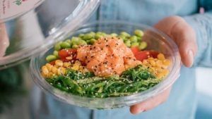 Una persona sostiene un colorido poke bowl del Restaurante Ibiza Poke, con salmón fresco, edamame, tomates cherry, maíz, algas y semillas de sésamo. - ForTwo - Planes para parejas
