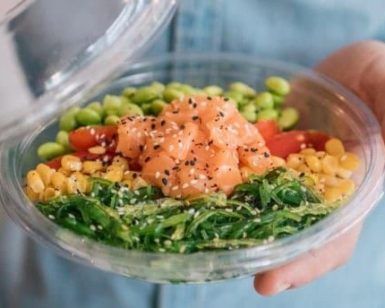 Una persona sostiene un colorido poke bowl del Restaurante Ibiza Poke, con salmón fresco, edamame, tomates cherry, maíz, algas y semillas de sésamo. - ForTwo - Planes para parejas
