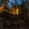 El Punta Espiñeiro, el lujo de Cabanas sem Barreiras en A Coruña, ofrece un escape sereno con una casa en el árbol elevada sobre pilotes entre los árboles, que brilla cálidamente a través de grandes ventanales al anochecer, proporcionando una tranquilidad similar a las acogedoras cabañas. - ForTwo - Planes para parejas
