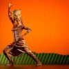 Un artista disfrazado de león captura la esencia del *Musical El Rey León en Madrid* en el escenario, con un fondo naranja y una escenografía verde vibrante, dando vida a la magia de este querido espectáculo. - ForTwo - Planes para parejas