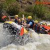 Un grupo de aventureros con casco experimentando la emoción del Rafting en el Río Genil - Aguas Bravas, navegando por las salpicadas aguas del río. - ForTwo - Planes para parejas