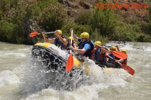 Un grupo de aventureros con casco experimentando la emoción del Rafting en el Río Genil - Aguas Bravas, navegando por las salpicadas aguas del río. - ForTwo - Planes para parejas