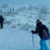 Gente haciendo senderismo con bastones de esquí y raquetas de nieve en una colina nevada en Navacerrada, Madrid, entre árboles helados bajo un cielo nublado durante la 'Excursión raquetas de nieve con luna llena'. - ForTwo - Planes para parejas