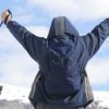 Con "Sobreviviendo a la nieve en la montaña (Andorra)" en la mano, un senderista levanta sus bastones triunfante, enmarcado por la impresionante montaña nevada y los árboles de Andorra. - ForTwo - Planes para parejas