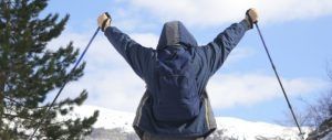 Con "Sobreviviendo a la nieve en la montaña (Andorra)" en la mano, un senderista levanta sus bastones triunfante, enmarcado por la impresionante montaña nevada y los árboles de Andorra. - ForTwo - Planes para parejas
