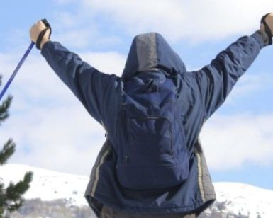 Con "Sobreviviendo a la nieve en la montaña (Andorra)" en la mano, un senderista levanta sus bastones triunfante, enmarcado por la impresionante montaña nevada y los árboles de Andorra. - ForTwo - Planes para parejas