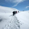 Un grupo disfruta de la Excursión con raquetas de nieve con las mejores vistas del Pedraforca (Vallcebre, Barcelona) mientras caminan bajo un cielo azul despejado, con el majestuoso Pedraforca alzándose a lo lejos. - ForTwo - Planes para parejas