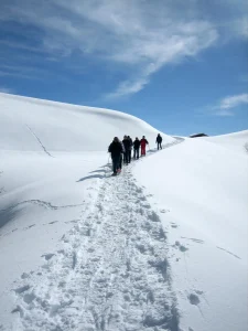 Un grupo disfruta de la Excursión con raquetas de nieve con las mejores vistas del Pedraforca (Vallcebre, Barcelona) mientras caminan bajo un cielo azul despejado, con el majestuoso Pedraforca alzándose a lo lejos. - ForTwo - Planes para parejas