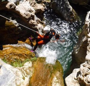 Usando un traje de neopreno, una persona desciende expertamente una cascada hacia una piscina rocosa, abrazando la emoción del Barranquismo en Granada - Tramo medio de Río Verde. - ForTwo - Planes para parejas