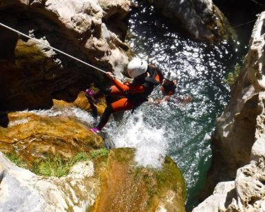 Usando un traje de neopreno, una persona desciende expertamente una cascada hacia una piscina rocosa, abrazando la emoción del Barranquismo en Granada - Tramo medio de Río Verde. - ForTwo - Planes para parejas